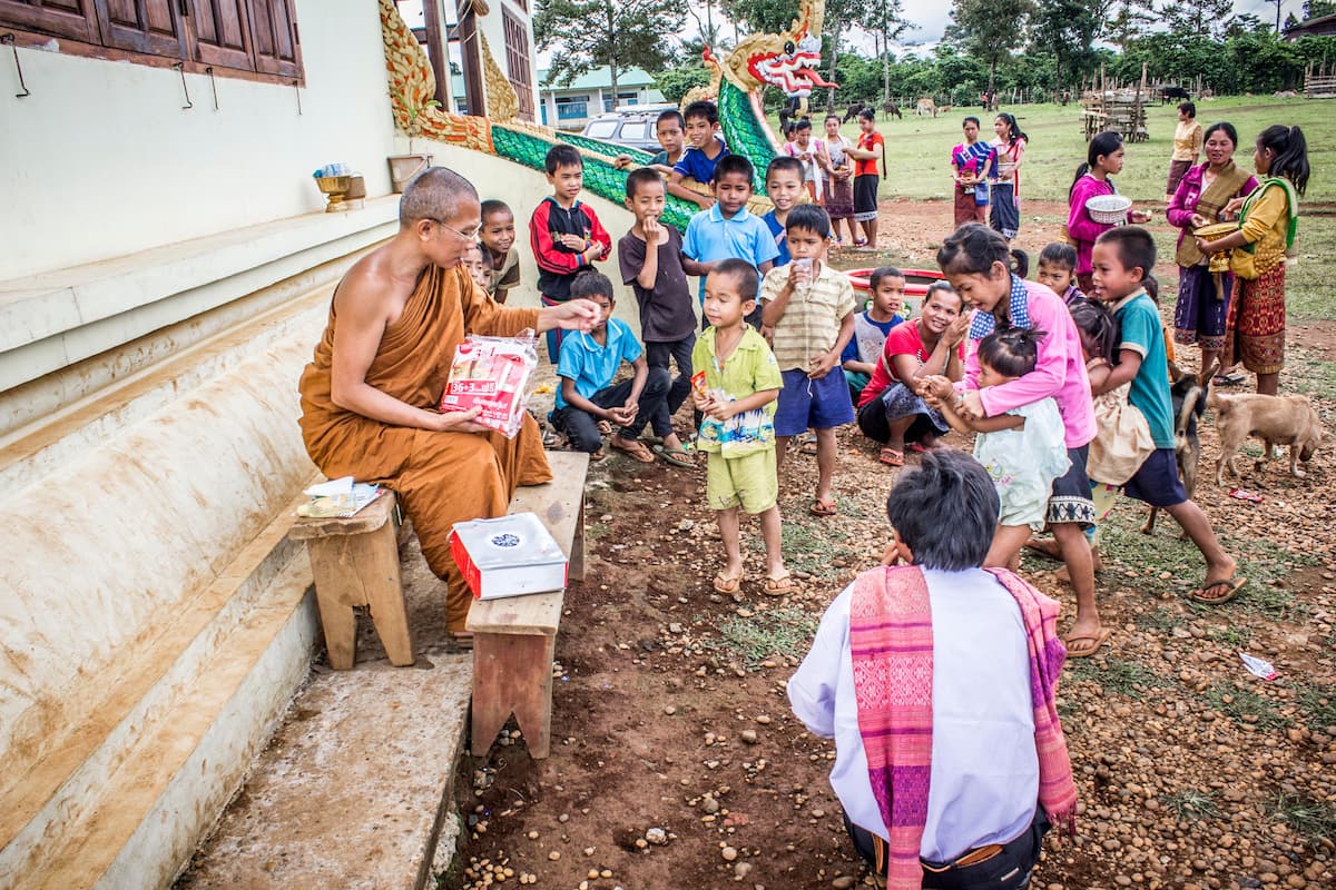 Buddhist monk with local families and children outside a temple in rural Thailand.