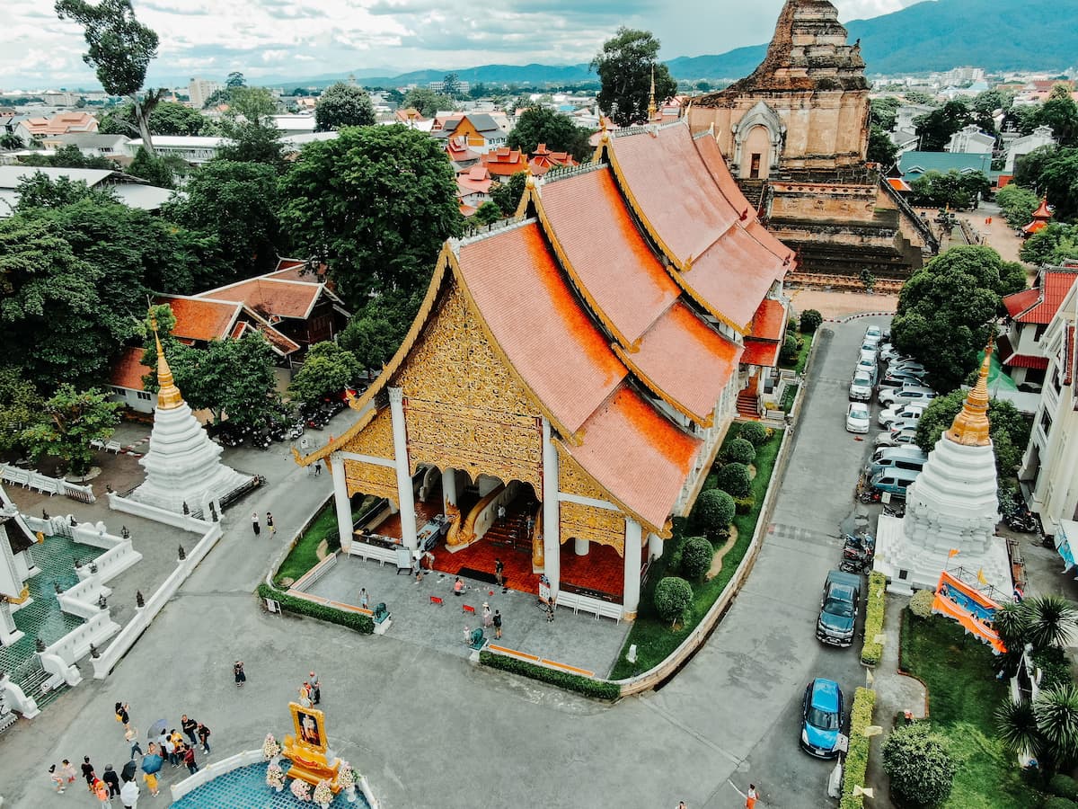 Wat Chedi Luang temple complex in Chiang Mai, Thailand, with traditional orange-roofed buildings and the historic brick chedi behind.
