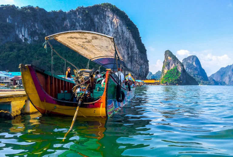 Colorful longtail boat floating on emerald green water with limestone cliffs in Phang Nga Bay, Thailand