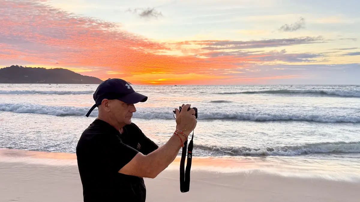 Dave Hibbins photographing a vivid sunset at Freedom Beach, Phuket, Thailand, with waves and golden reflections on the sand
