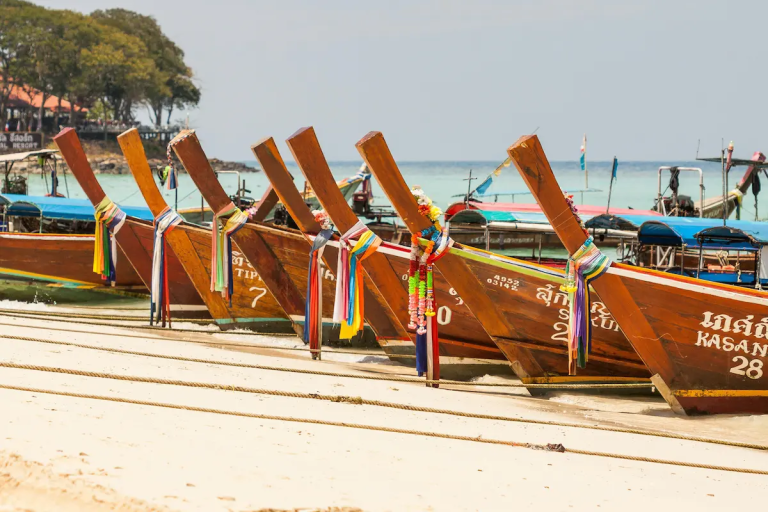 Row of decorated longtail boats on a sandy Thai beach with turquoise sea in the background