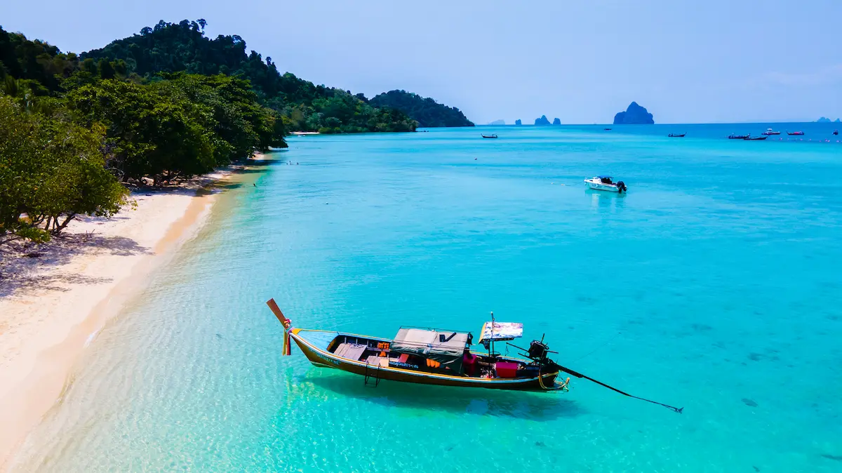 Longtail boat floating in clear turquoise water off Koh Kradan’s beach in Trang, featured in the Complete Thailand Islands Guide.