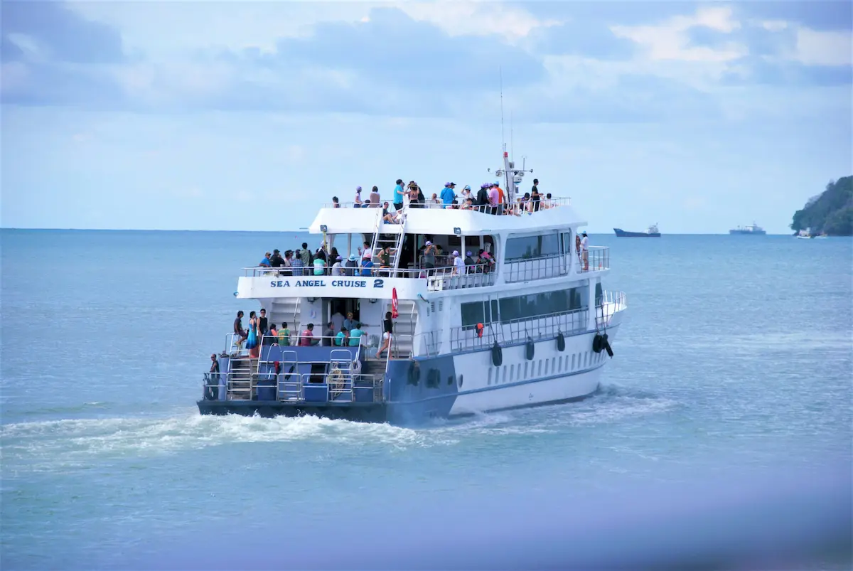 A packed white ferry named Sea Angel Cruise 2 sailing away from Phuket with passengers on deck under a bright blue sky.