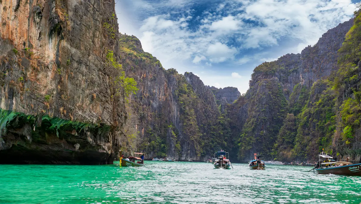 Longtail boats entering Pileh Lagoon during a phi phi islands tour from Phuket, surrounded by towering limestone cliffs and turquoise water