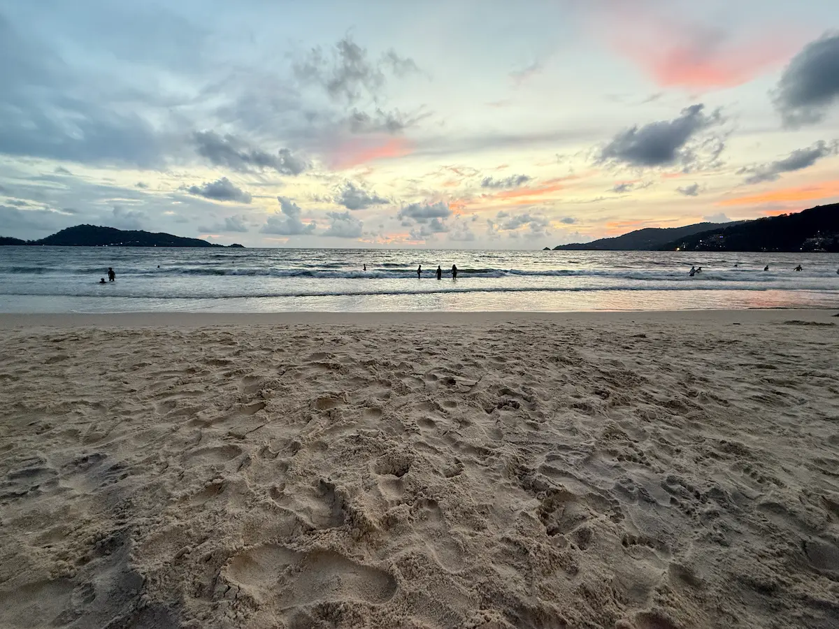 People walking and swimming at Patong Beach in Phuket during the day with waves and shoreline