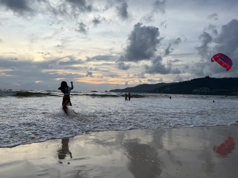 Person running through waves at Patong Beach Phuket with parasailing and shoreline in background