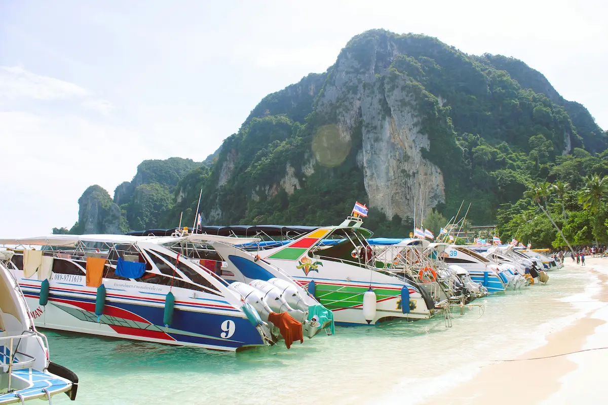 Phi Phi islands tour Phuket with speedboats lined up on beach and limestone cliffs