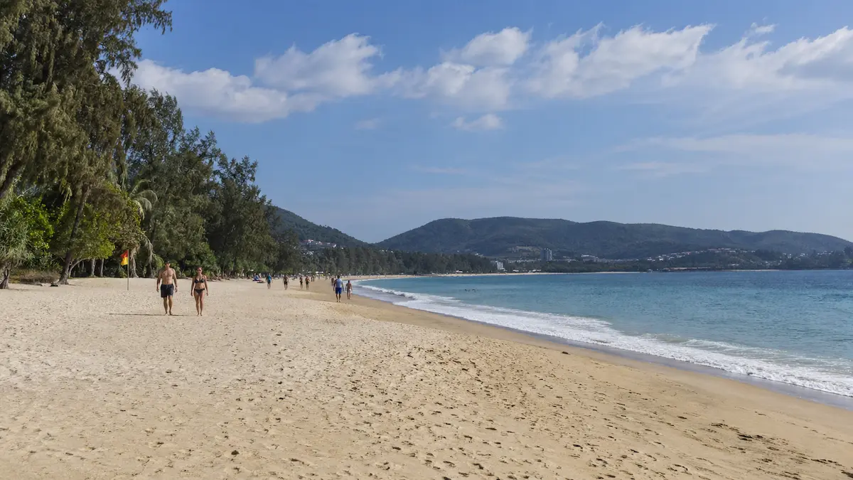 Bang Tao vs Surin Phuket guide showing the wide sandy shoreline of Bang Tao Beach with calm sea and open space for walking.