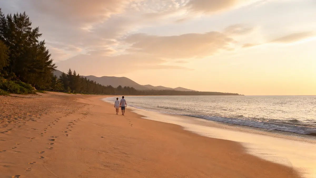Couple walking along Mai Khao Beach in Phuket Thailand at sunset with wide sandy shoreline and calm sea