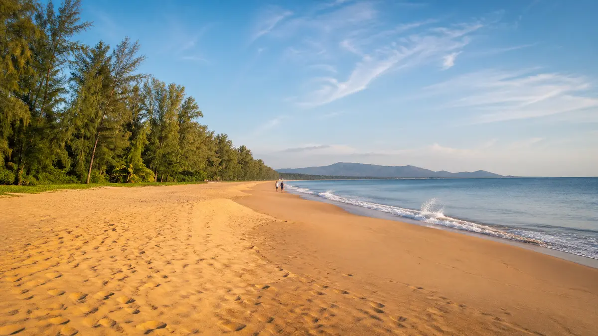 Mai Khao Beach in Phuket Thailand showing a long quiet sandy shoreline with tropical trees calm sea and spacious beach atmosphere