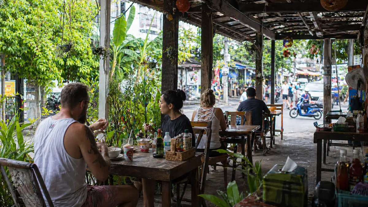 Patong Beach Phuket casual open-air cafe scene often featured in a Patong Beach guide, with tourists eating near the street and tropical surroundings