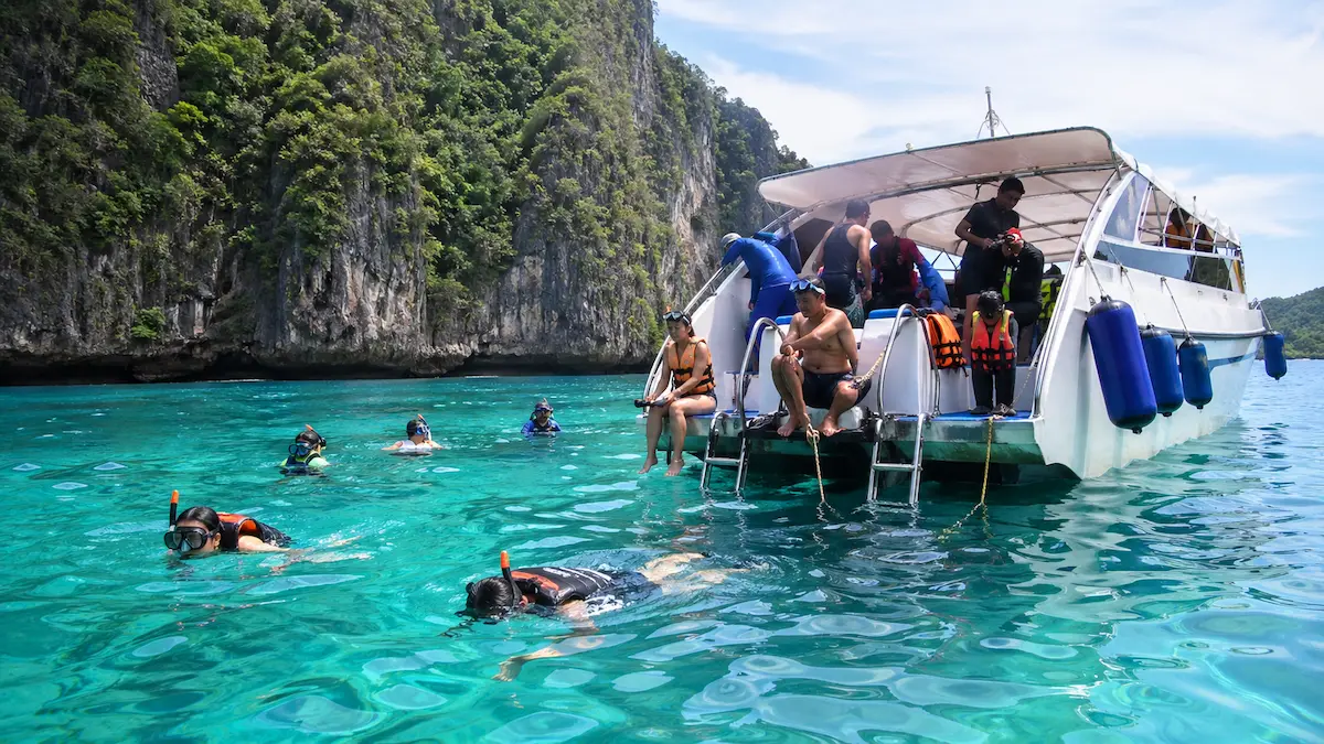 Travelers snorkeling during a Phi Phi island tour from Phuket beside tour boat in clear tropical water