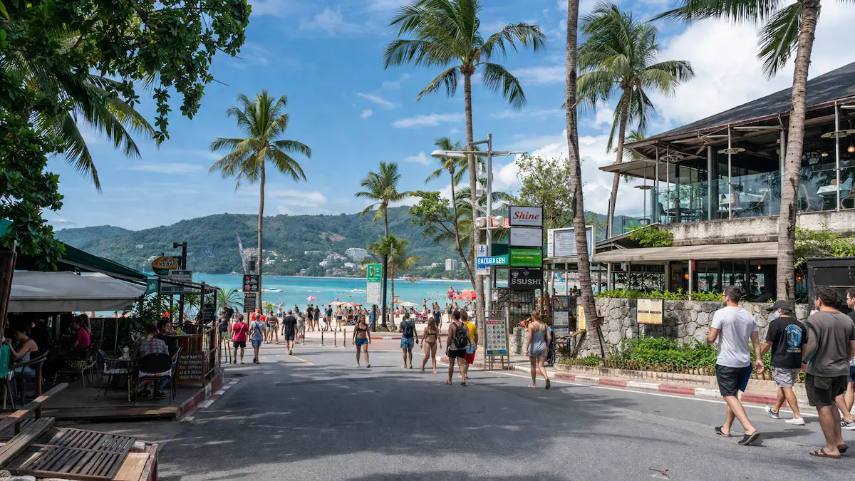 Street leading to Phuket beach with cafés, tourists, palm trees and lively tropical holiday atmosphere