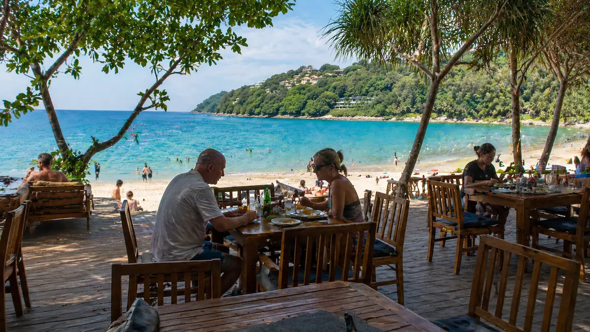 Beachfront dining near Surin Beach Phuket with travellers eating beside the sand and ocean during daytime