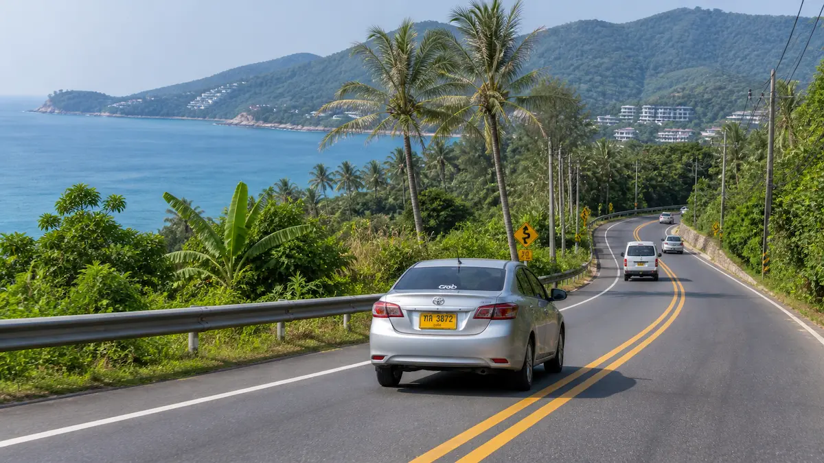 Getting around Phuket by car on a coastal road between beaches with sea and hills in the background