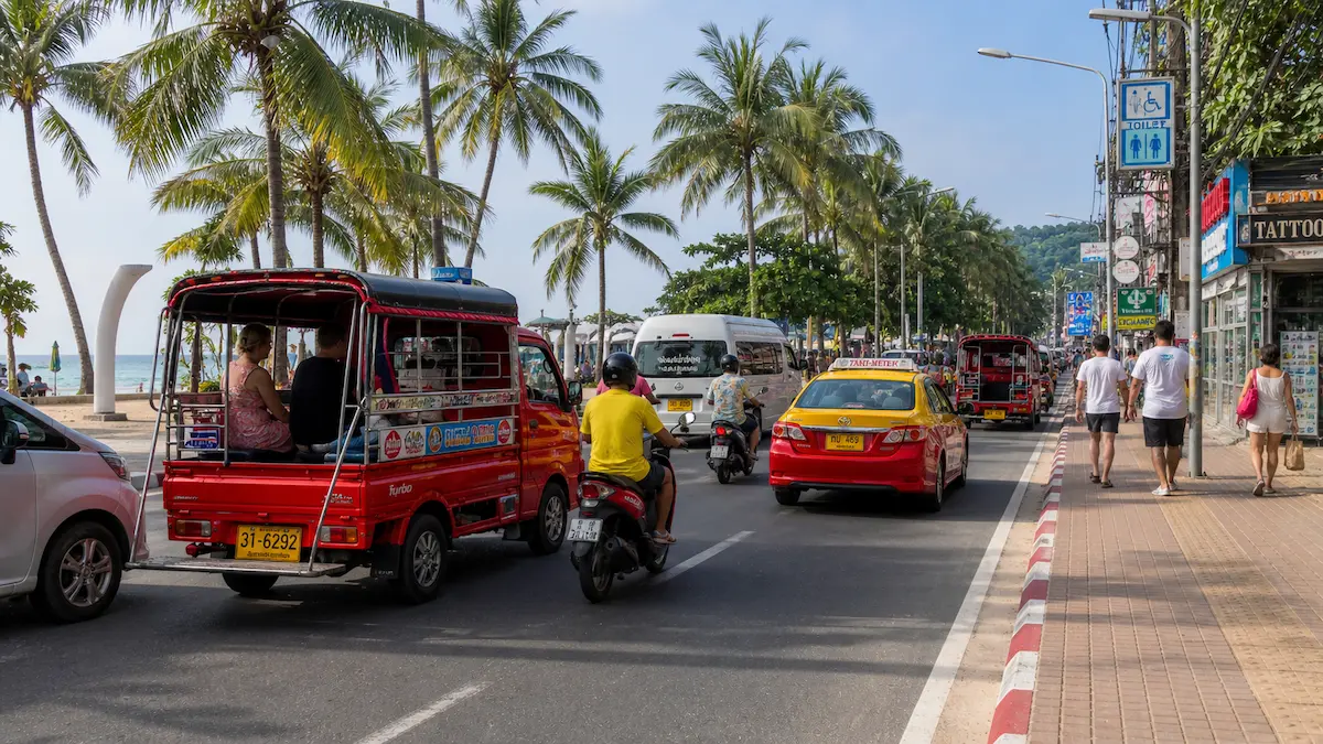 Getting around Phuket with Phuket-style tuk tuks, taxis, and scooters on a busy beachside road in Patong
