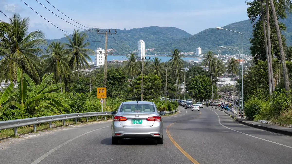 Phuket airport transfer car driving along tropical road toward Patong with hills and coastline