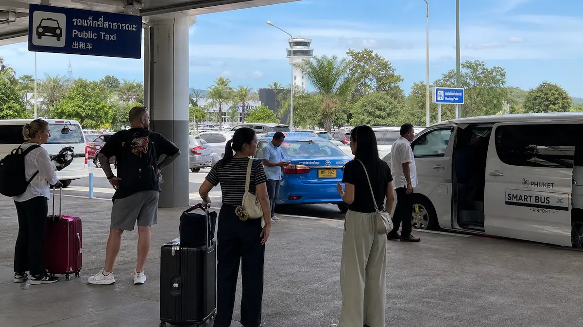 Phuket airport transfer taxi and bus pickup area with travellers waiting outside the terminal