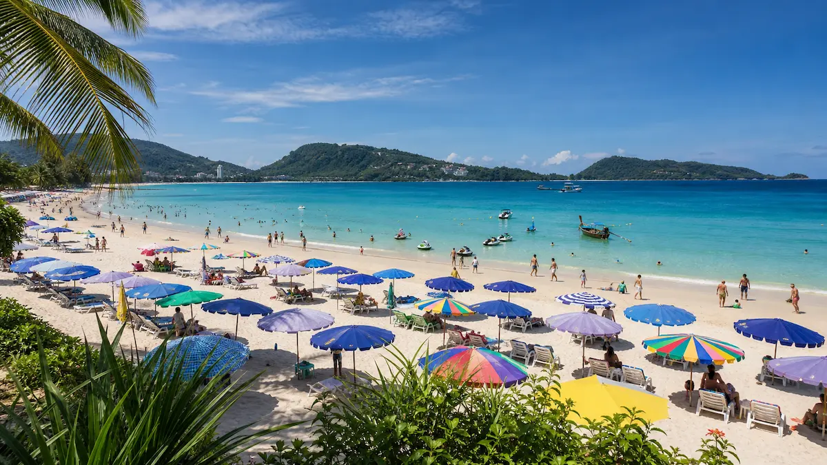 Phuket beach daytime scene with umbrellas, swimmers and clear turquoise water on a busy shoreline