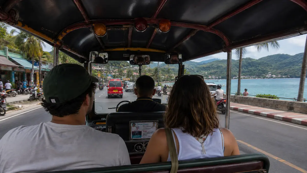 Tourists riding inside a Phuket tuk tuk along a coastal road in Thailand