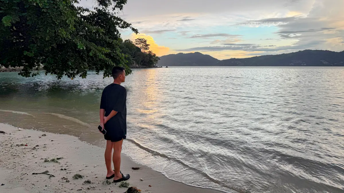 Person standing quietly on a calm Phuket beach during sunset in Thailand