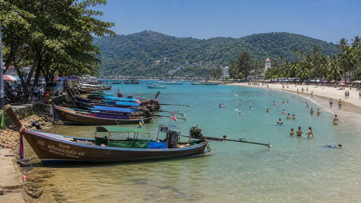 Rawai vs Nai Harn showing longtail boats at Rawai beach and swimmers at Nai Harn beach in Phuket