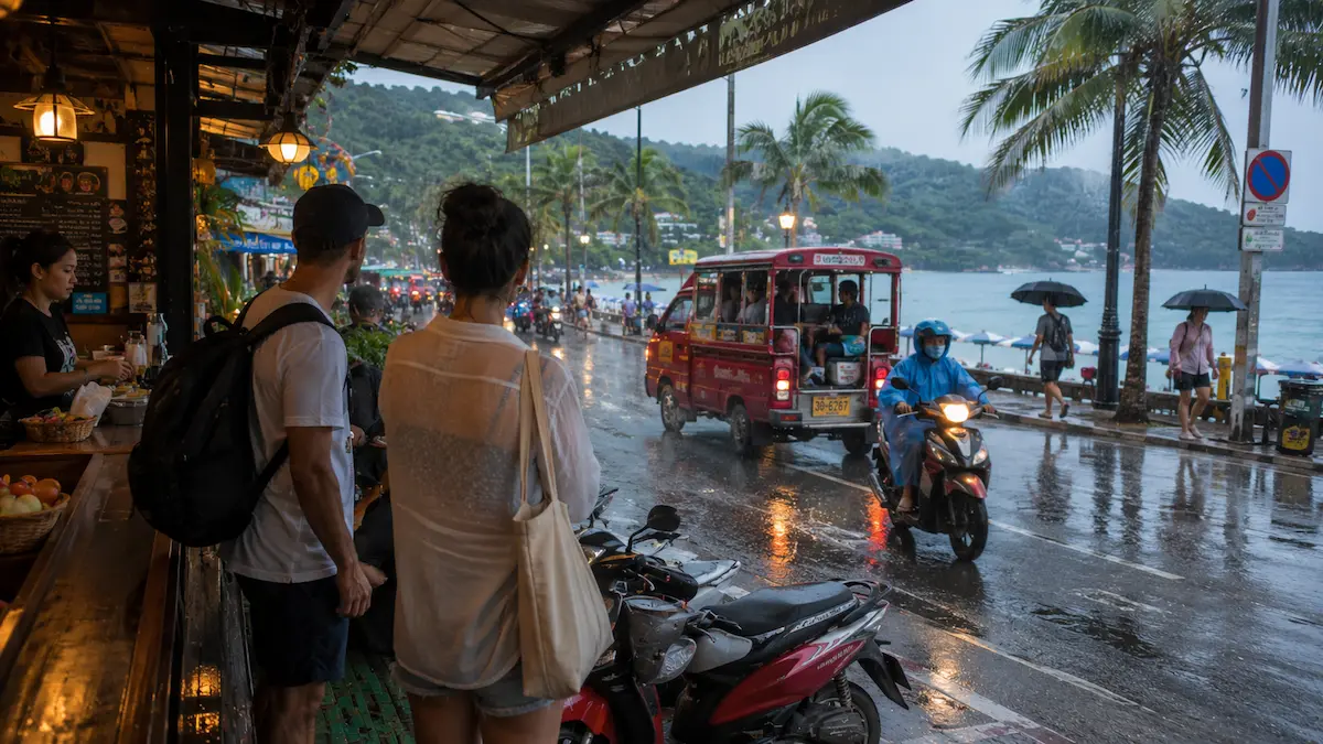 Travellers sheltering from tropical rain beside a busy Phuket beach road in Thailand