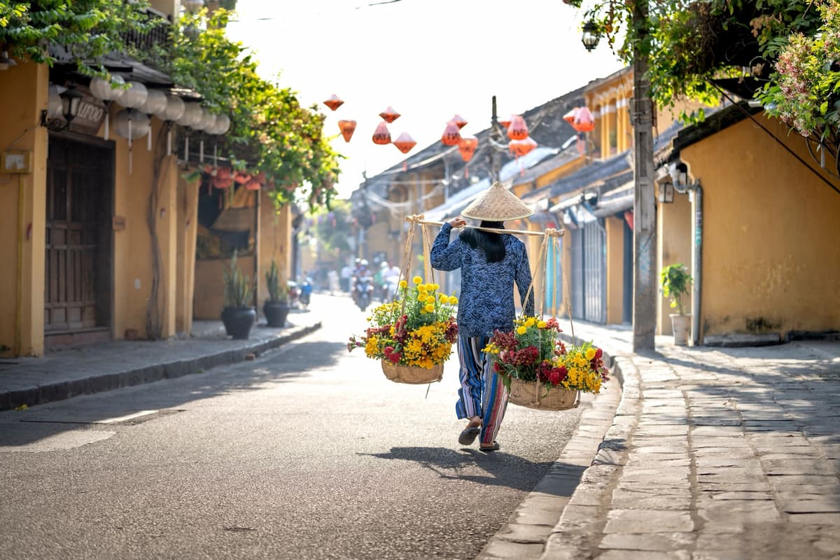 Go Find Asia – flower seller walking through the historic streets of Hoi An, Vietnam